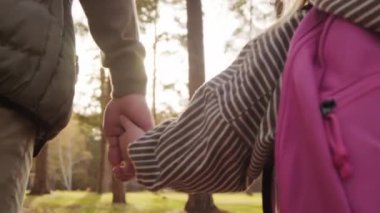 Küçük bir kızın elini tutan ve güneşli bir sonbahar gününde parkta onunla yürüyen tanınamayan babaların yavaş yavaş yakınlaşması.