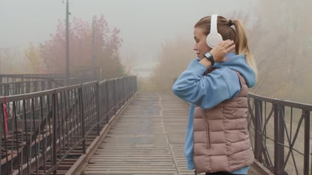 Langzaam Schot Van Jonge Vrouw Hoodie Opgeblazen Vest Zet Koptelefoon — Stockvideo