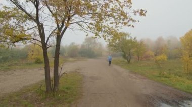 Sonbaharın sisli sabahında parkta koşan mavi kapüşonlu genç kadının yavaş yavaş izini sürüyorum.