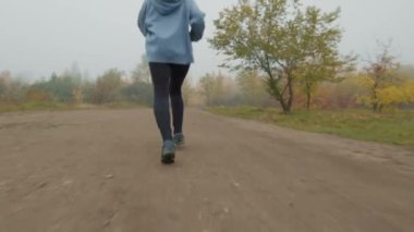 Yavaş yavaş, sisli bir sonbahar gününde parkta koşan kapüşonlu genç bir kadının dikiz aynasından takip ediliyor.