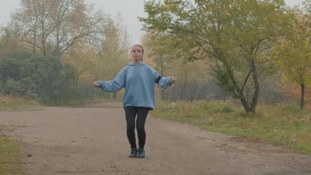 Kapüşonlu Genç Bir Kadının Sisli Bir Sonbahar Sabahında Parkta Atlama — Stok video