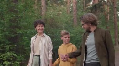 Yazın ormanda gezinen, sohbet eden ve eğlenen üç kişilik mutlu beyaz bir ailenin orta boy fotoğrafı.