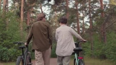 Düşük açılı, orta açılı, genç ve sağlıklı bir çiftin ormanda bisikletle yürürken konuştuğu görüntüler.