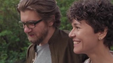 Yazın yeşil bir ormanda doğanın tadını çıkarırken gülümseyen ve konuşan neşeli beyaz çiftin el ele çekilmiş fotoğrafı.