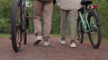 Düşük kesimli arka plan görüntüleri. Sıradan kıyafetler ve spor ayakkabılar giymiş, bisiklet taşıyan bir çift bacak.