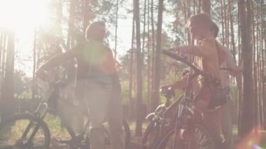Bisikletle ormanda dinlenen, sohbet eden ve yaz tatilinin tadını çıkaran üç kişilik beyaz bir ailenin düşük açılı görüntüsü.