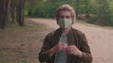 Beyaz adamın, boş orman yolunda durup pamuk maskeyi çıkarırken kameraya gülümseyen orta ölçekli portresi.