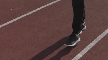 Siyah eşofmanlı, omuz çantalı, yaz aylarında pistte yürürken çekilen beyaz kadın atlet.