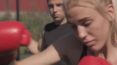 Yazın spor sahasında erkek antrenörle boks antrenmanı yapan genç atletik kadının yakın çekimi.