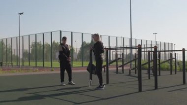 Siyah eşofmanlı genç çiftin spor sahasında antreman yapıp sohbet edip ısındığı bir fotoğraf.