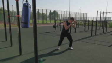 Güneşli bir günde spor sahasında tek başına boks yapan beyaz bir adam.