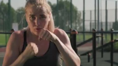 Genç güçlü bir kadının belden aşağısı. Yazın spor sahasında boks antrenmanı yapan kameraya bakıyor.