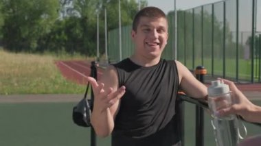 Omzunun üstünden genç ve enerjik bir adamın, yaz aylarında spor sahasında barda birlikte antrenman yaptığı bayan arkadaşıyla konuştuğu orta boy bir fotoğraf.