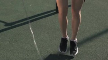 Yazın spor sahasında antrenman yaparken şort atlayan, siyah etekli, beyaz, çekici genç bir kadının eğik portresi. Sonra da gülümseyen kameraya bakıyor.