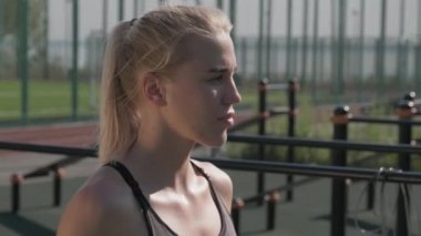 Genç çekici atletik kadının kulaklık takıp güneşli bir yaz gününde spor sahasında boks yapmaya başlamasının orta ölçekli yan görüntüsü.