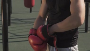 Konsantre olmuş genç bir sporcunun belden yukarı vuruşu. Yazın spor sahasında duran boks eldivenleri giyiyor.