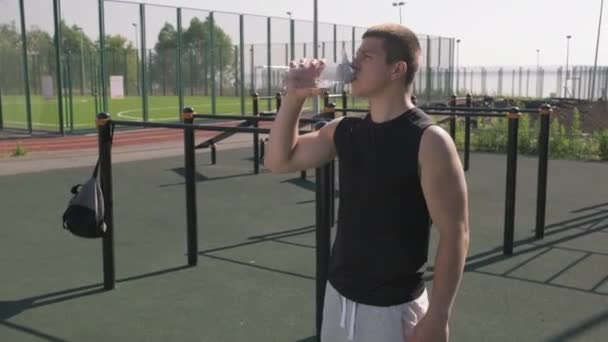 手持中镜头 年轻运动员站在运动场外 从体育瓶子中喝水 — 图库视频影像