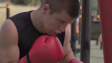 Açık hava spor sahasında boksör boksör boks çantasının orta boy portresi. Sonra da kameraya bakıyor.