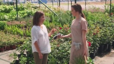 Yavaş çekimde bir kadın yazın bahçenin dışında ev bitkileri satın alıyor ve onlara ulaşılamaz kredi kartıyla ödeme yapıyor.