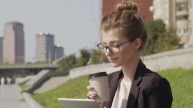 Nehir kenarında çalışırken yaz tatili kahvesini yudumlayan gözlüklü çekici genç bir kadının yavaş çekim görüntüsü.