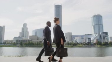 Güneşli bir günde nehir kenarında yürüyen çok ırklı iş çiftlerinin yavaş çekimde dikiz aynasından çekimleri.