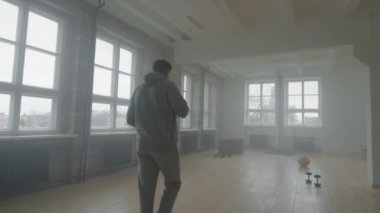 Gri eşofmanlı kendini adamış bir afro sporcunun boş bir çatı katında ağır antrenmana hazırlanırken ceketini çıkarmasıyla çekilen dikiz görüntüsü. Spor motivasyonu kavramı