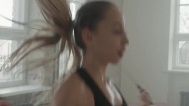 Tebeşir tozu dumanıyla dolu çatı katı tarzı spor salonundaki halat eğitimini atlayarak kardiyo egzersizi yapan çekici genç bir kadının orta ölçekli yakın çekimi.