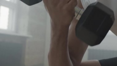 Afrika kökenli Amerikalı sporcunun dambılı dumanlı çatı katı tarzı spor salonu stüdyosunda egzersiz yaparken yavaş çekimde.