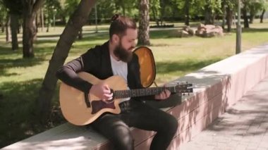 Sakallı, parktaki uzun sırtüstü bankta oturup gitarla şarkı söyleyen ve sonra da kameraya bakan erkek sokak müzisyeninin portresini çekiyorum.