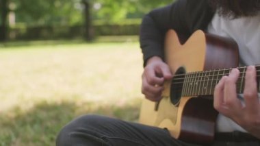 Tanımlanamayan sakallı adamın yaz günü parkta akustik gitar çalmasını yakından çekiyoruz.