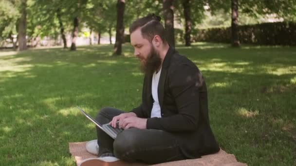 Sledování Záběr Mladého Muže Vousy Sedí Přikrývce Zelené Trávě Parku — Stock video