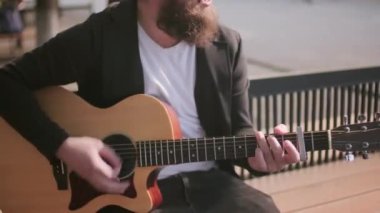 Şehirde bankta oturan ve akustik gitarla şarkı söyleyen neşeli sokak müzisyenlerine yakın durun.