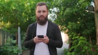 Dışarıda yürüyen ve cep telefonuyla yazan sakallı şık bir gencin fotoğrafını çekiyorum.