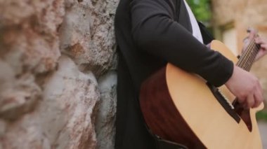 Dışarıda duvara yaslanıp akustik gitar çalan tanınmayan bir erkek müzisyenin yavaş çekim çekimini kapat.