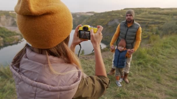 明るい父と5歳の息子の写真を撮る若い女性の手持ち撮影採石場の湖を見下ろす緑の丘の上にポーズ — ストック動画