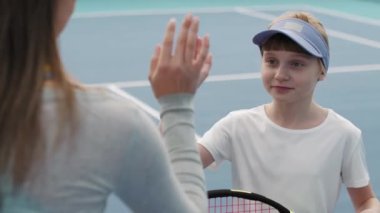Genç bayan tenis koçunun yavaşlığıyla omuz üstünden orta vuruş tenis kortunda birlikte duran küçük kıza beşlik çakıyor.