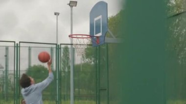 Dışarıda basketbol oynarken hoplayıp zıplayan ve topu potaya atan genç adamın el bilgisayarı yavaş yavaş takibi.