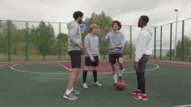 Kasvetli bir günde sokak basketbolu oynamadan önce dışarıda yazı tura atan mutlu genç adamların orta boy fotoğrafı.