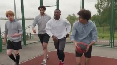 Dört mutlu gencin top sürerken, basketbol sahasında koşarken, basket atarken ve ısınırken çekilen görüntüler.