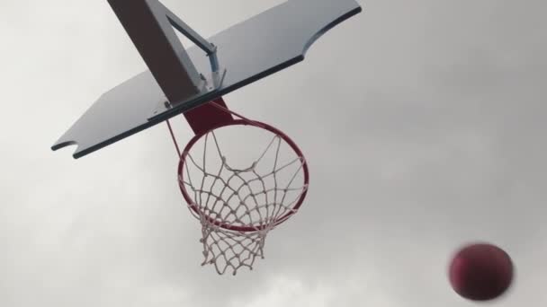 暗い日に屋外バスケットボールコートのフープに投げられるボールの低角度ショット — ストック動画