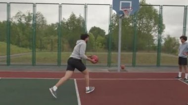 Rastalı mutlu bir adamın el kamerasıyla dışarıdaki basketbol sahasında topu potaya fırlatırken çekilen fotoğrafı. Gol atıyor ve arkadaşları ona tezahürat yapıyor.