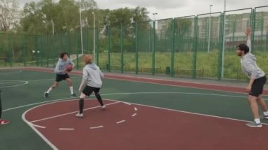 Dışarıda basketbol sahasında sokak basketbolu oynayan kapüşonlu bir grup gencin el kamerasıyla çekilmiş fotoğrafı.