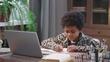 Dizüstü bilgisayarla çalışıp kameraya gülümseyen 8 yaşındaki afro-amerikalı çocuğun belden yukarı pozu.