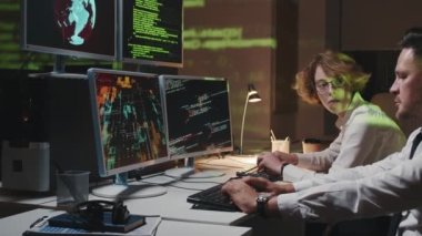 Olgun Kafkasyalı erkek ve genç kadın ofiste geç saatlere kadar kalıp bilgisayar korsanlarının saldırısını önlemeye çalışıyorlar.