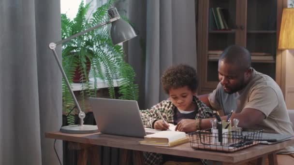 潘宁拍了一半的非洲裔美国人的照片 他们一起坐在客厅的桌子前帮助他可爱的小儿子做功课 — 图库视频影像