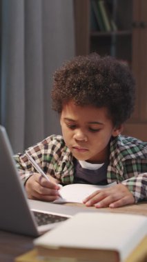 Evinden bilgisayarına bakarak kitap yazan akıllı afro çocuğun dikey yakın plan fotoğrafı.