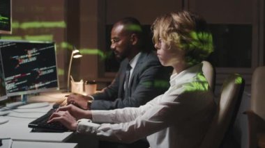 Ciddi bir erkek ve kadının geç saatlere kadar çalışıp bilgi güvenlik yazılımlarını güncellediği yan görüntü.