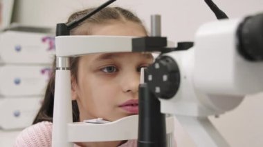 Küçük kızın göz kontrolü yaparken göz doktorunun muayenehanesindeki fosfobik makineden bakarken orta ölçekli görüntüsü.