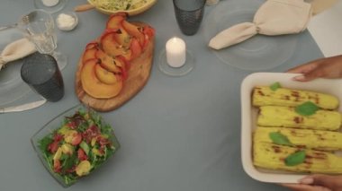 Bayramlık yemek masasında koçanlarda kavrulmuş mısır servis eden tanınmamış kadın elleri ve mumlar.