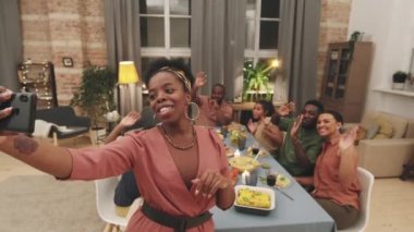 Orta büyüklükte Afro-Amerikalı bir kadının akıllı telefonu elinde tutarak kameraya gülümserken kameraya çektiği fotoğraf.